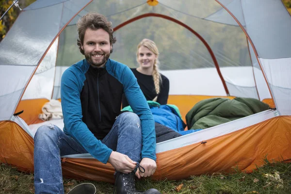 Мужчина завязывает шнурок, а женщина отдыхает в палатке — стоковое фото