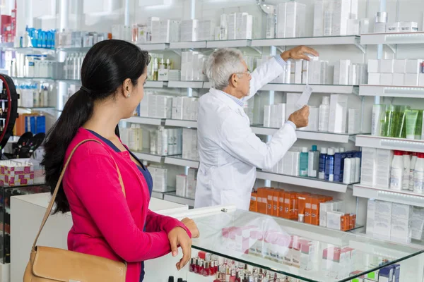 女人看着化学家寻找在货架上的药 — 图库照片