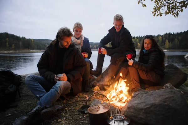 Freunde mit Kaffeetassen sitzen am Lagerfeuer — Stockfoto