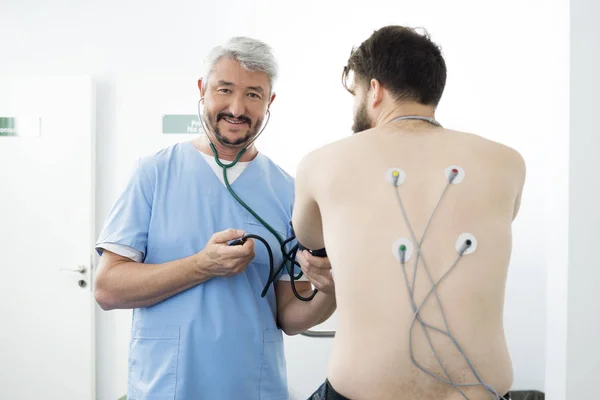 Médico sorridente medindo a pressão arterial do paciente no hospital — Fotografia de Stock