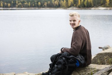 Lakeshore üzerinde oturan mutlu erkek uzun yürüyüşe çıkan kimse