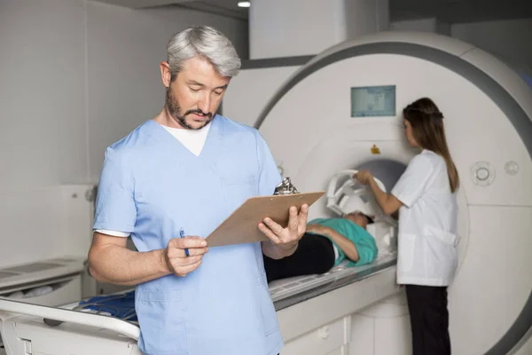 Doctor leyendo portapapeles con colega preparando paciente para ct — Foto de Stock