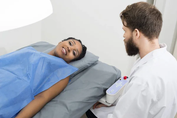 Paciente deitado na cama enquanto o médico está sentado na clínica — Fotografia de Stock