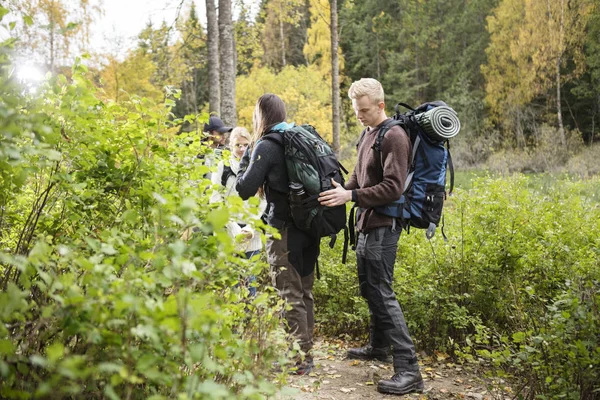 Uomo regolazione zaino di amico durante escursione in foresta — Foto Stock