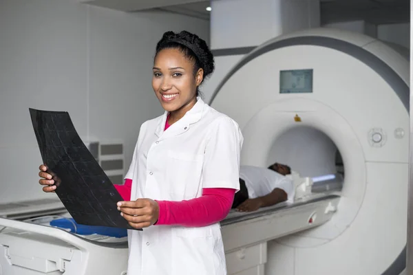 Arzt hält Röntgenbild in der Hand, während Patient auf Scanner liegt — Stockfoto