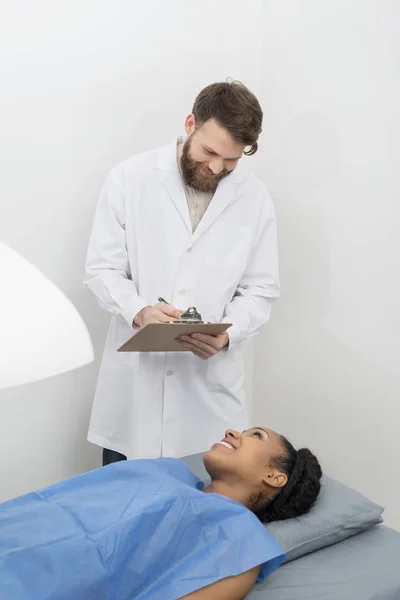 Médico escrevendo na área de transferência enquanto paciente submetendo osso Densit — Fotografia de Stock