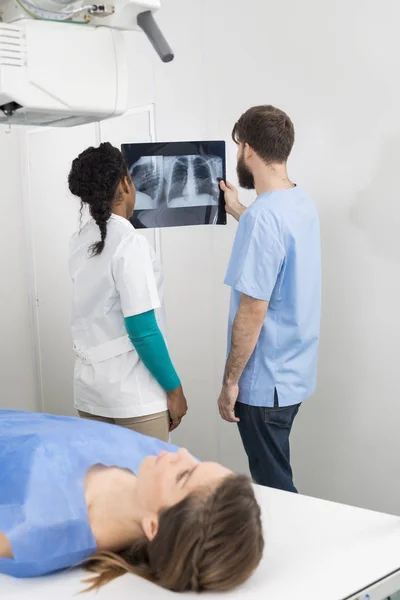 Radiologistas analisando raio-X com mulher deitada em primeiro plano — Fotografia de Stock