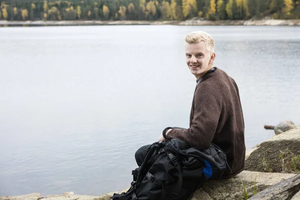 Hombre feliz excursionista sentado en la orilla del lago — Foto de Stock