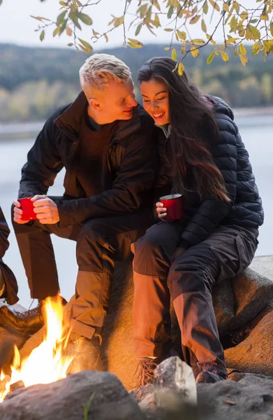Par med kaffekoppar som sitter nära lägerelden — Stockfoto