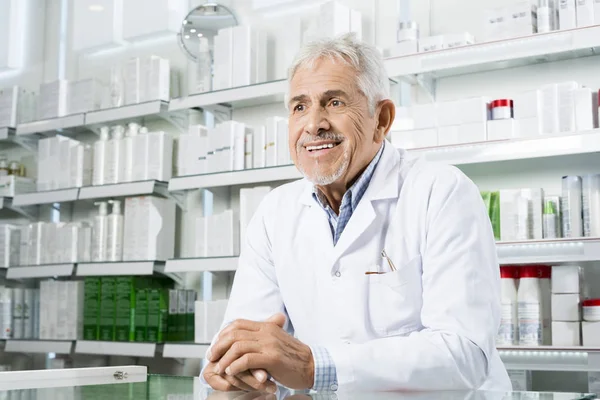 Farmacêutico olhando para longe enquanto se inclina no contador — Fotografia de Stock