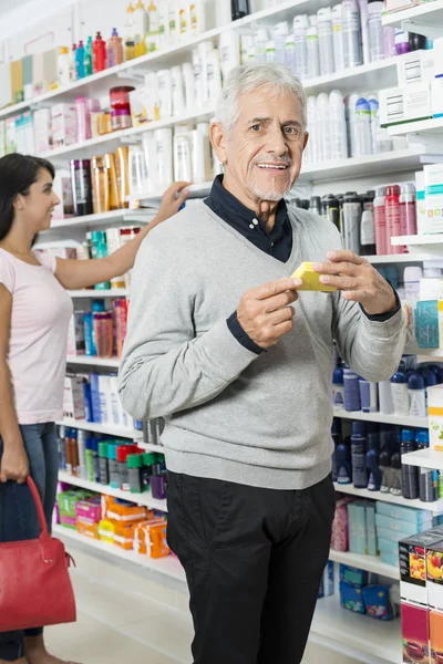 Старший чоловік тримає продукт, а жінка купує в аптеці — стокове фото