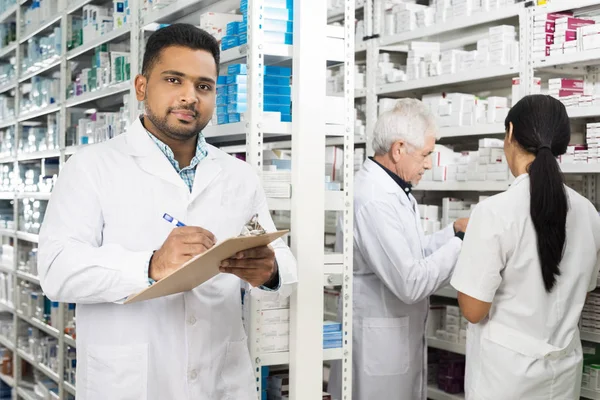 Químico Confiado Escribiendo En Portapapeles Mientras Sus Colegas De Pie — Foto de Stock