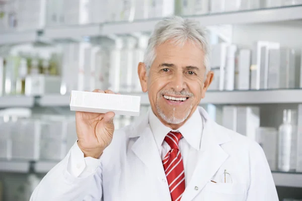 Lachende apotheker geneeskunde vak houden tegen planken — Stockfoto