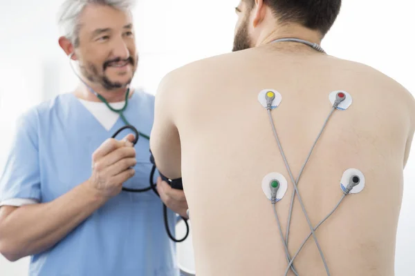 Médico examinando paciente con electrodos conectados en la espalda en Os — Foto de Stock