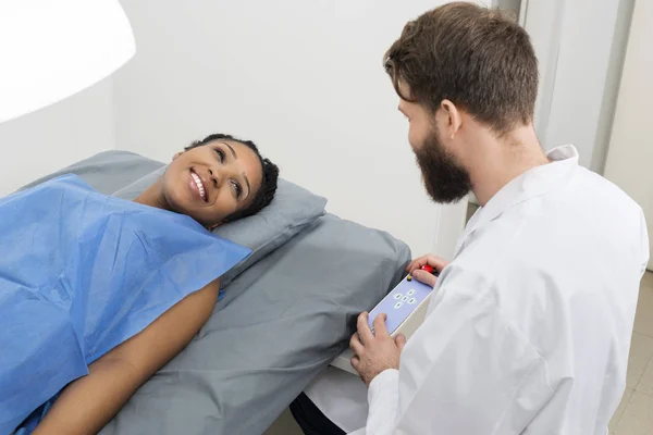 Женщина смотрит на врача мужского пола, осматривая ее в клинике — стоковое фото