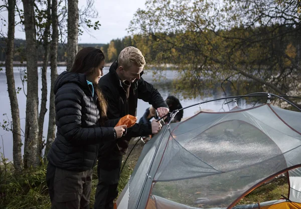 Unga par inställningen upp tält vid sjön — Stockfoto