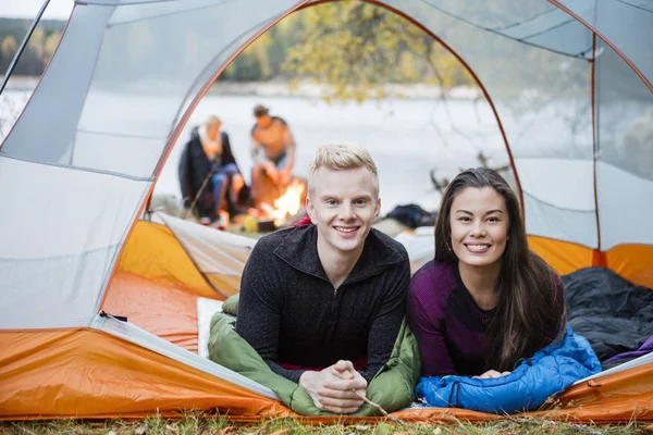 Casal jovem deitado na tenda durante o acampamento à beira do lago — Fotografia de Stock