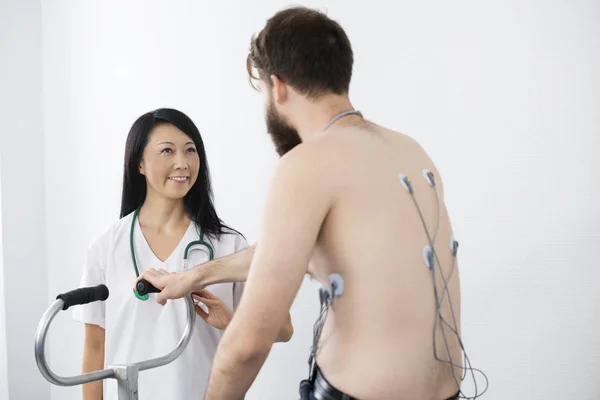 Médico olhando para o paciente de bicicleta com eletrodos ligados em Ba — Fotografia de Stock
