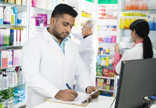 Químico escribiendo en portapapeles mientras sus colegas trabajan en Pharmac —  Fotos de Stock