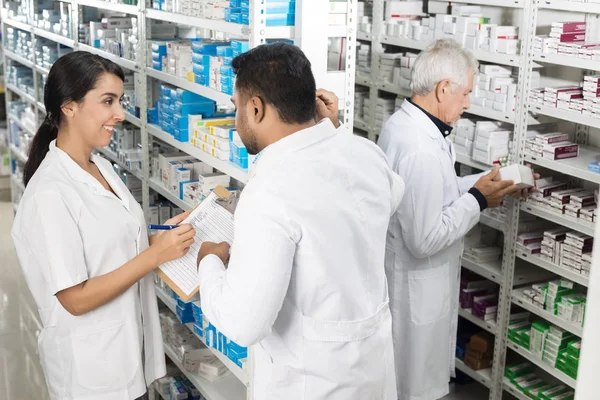 Farmacêuticos que trabalham por prateleiras na farmácia — Fotografia de Stock