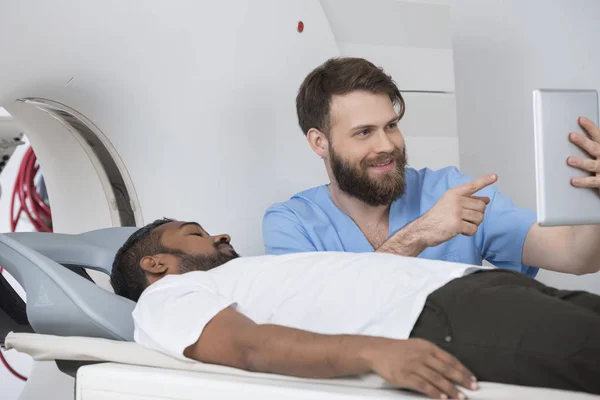 Medico che mostra la compressa digitale al paziente che giace sull'analizzatore CT — Foto Stock