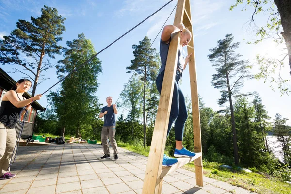 Amigos masculinos y femeninos tirando de cuerdas para equilibrar a la mujer en madera — Foto de Stock