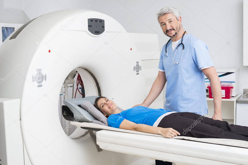 Doctor Standing By Patient Lying On MRI Machine