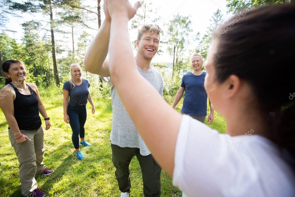 Man And Woman Giving High-Five While Friends Standing At Forest