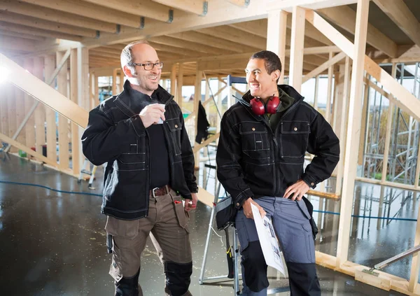 Colegas con plan y taza de café sonriendo en el sitio de construcción —  Fotos de Stock