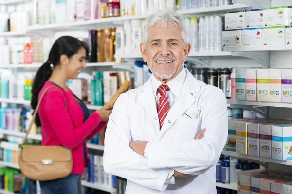 Lächelnder Apotheker mit verschränkten Armen, während sich der Kunde für pr — Stockfoto