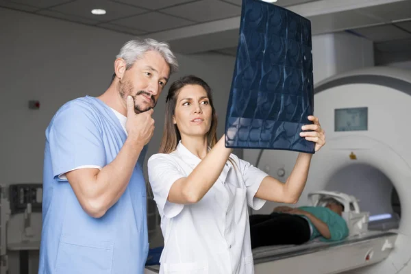 Ärzte untersuchen Röntgenbild mit Patient, der auf CT-Gerät liegt — Stockfoto