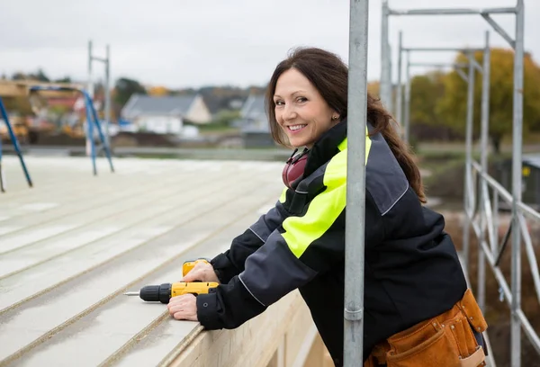 Női Carpenter mosolyogva, miközben a gazdaság fúró gép, a tető — Stock Fotó