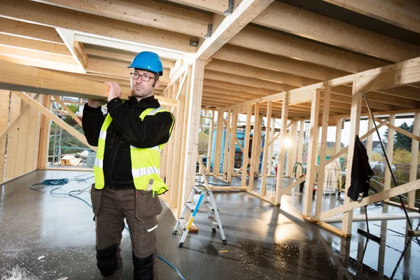 Omuz sitesinde odun taşıyan koruyucu ceketli bir marangoz