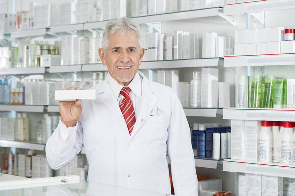 Pharmacist Holding Medicine Box Against Shelves