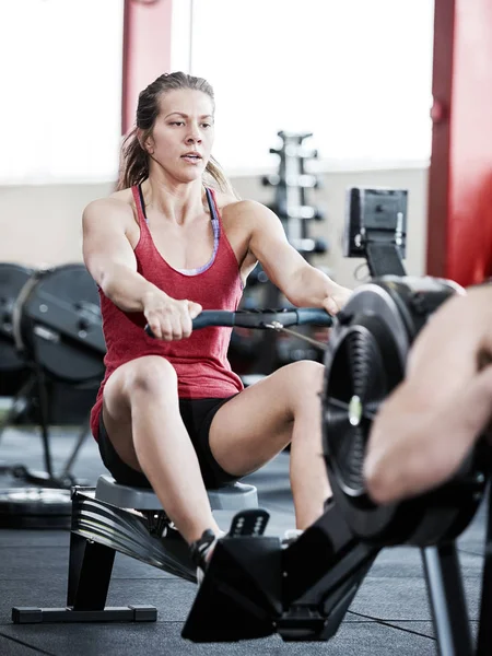 Donna che utilizza la macchina da canottaggio in palestra — Foto Stock