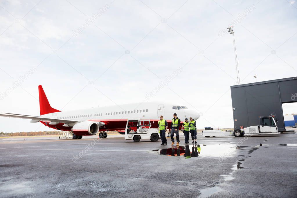 Workers Walking By Airplane On Wet Runway