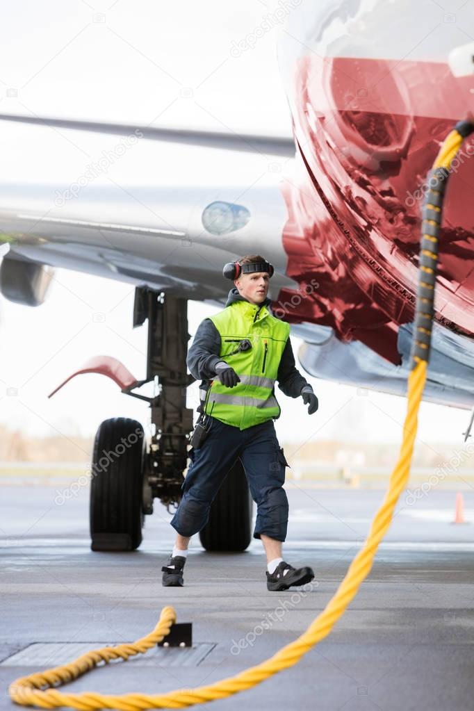 Crew Member Walking By Airplane Being Charged On Runway