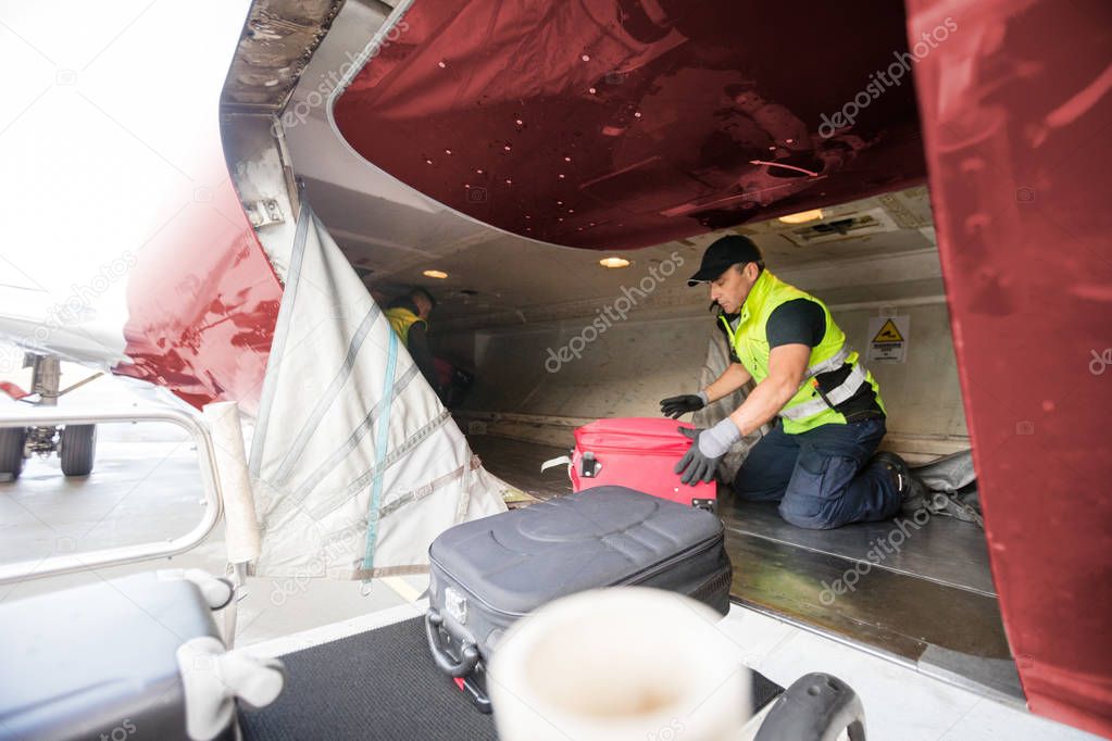 Worker Kneeling While Unloading Airplane