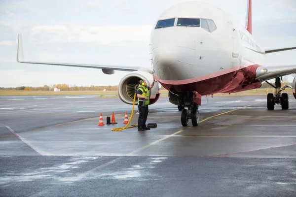 Рабочий заряжает самолет на мокрой взлетно-посадочной полосе аэропорта — стоковое фото