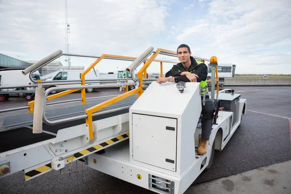 Travailleur confiant assis sur un camion de convoyeur à bagages — Photo
