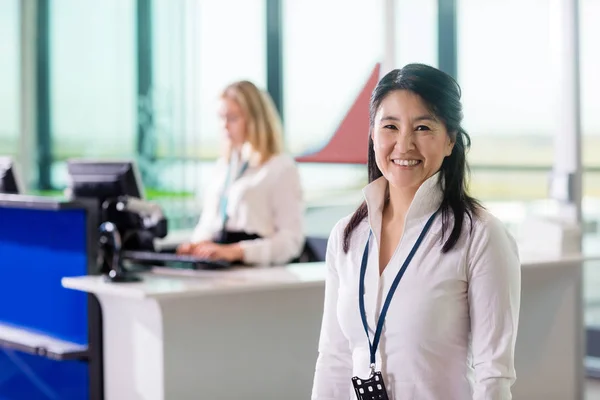 Персонал улыбается, когда коллега работает на стойке регистрации аэропорта — стоковое фото
