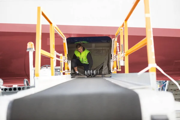 Trabalhador agachado em avião com transportador de bagagem em primeiro plano — Fotografia de Stock