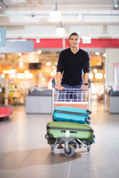 Handsome Young Man With Luggage In Cart At Airport