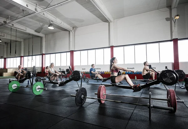 Atletas femeninos y masculinos usando máquina de remo — Foto de Stock