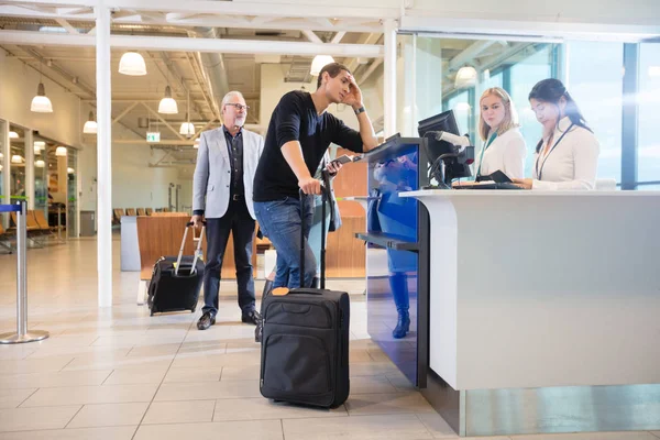 Сотрудники проверяют паспорт мужчины-пассажира на стойке в аэропорту — стоковое фото
