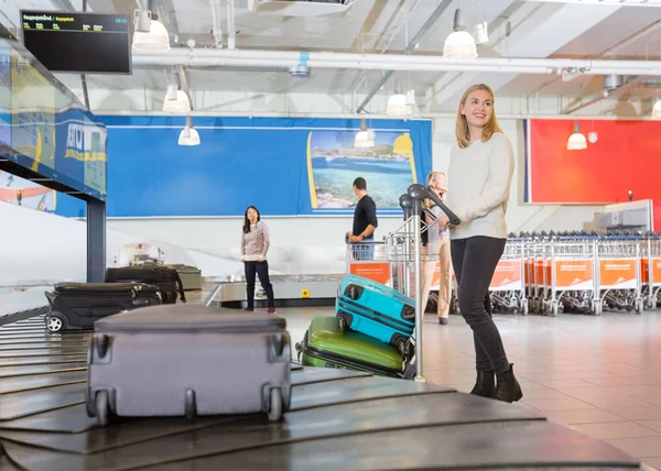 Kvinna med vagn stående av transportband på flygplats — Stockfoto