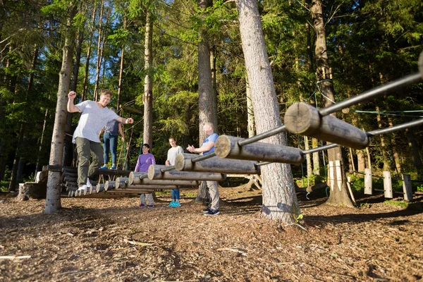 Amigos assistindo homem cruzando log ponte na floresta — Fotografia de Stock