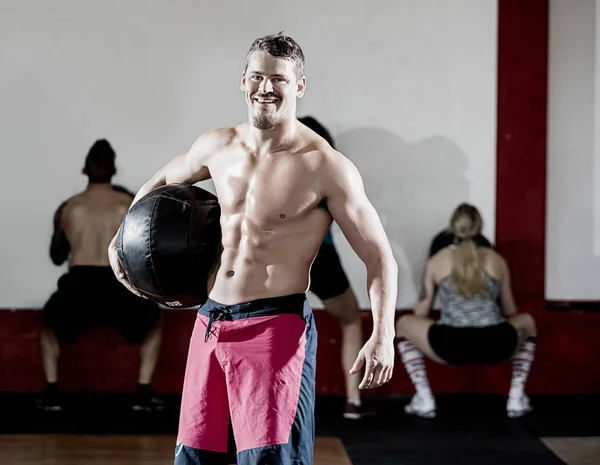 Hombre muscular sosteniendo balón de medicina mientras los clientes hacen ejercicio — Foto de Stock