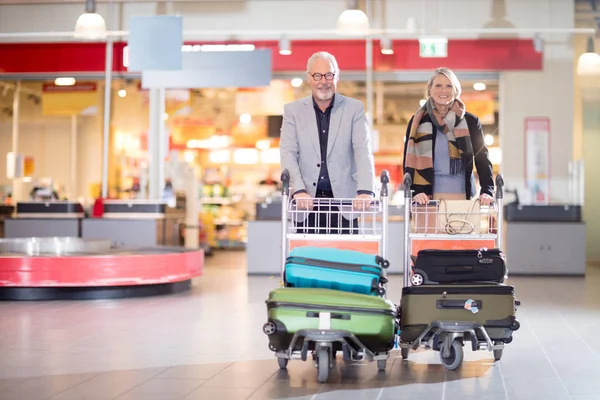 Heureux couple d'affaires senior avec bagages dans des chariots à l'aéroport — Photo