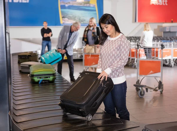 Женщина, собирающая багаж на транспортерном поясе в аэропорту — стоковое фото